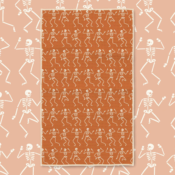 An orange rectangular rug with a repeating pattern of white dancing skeletons, centered on a peach background with a matching skeleton border.